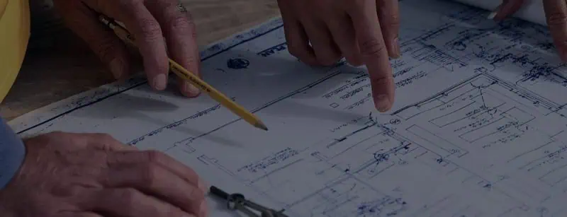 Close-up of hands sketching on a construction blueprint during a planning discussion