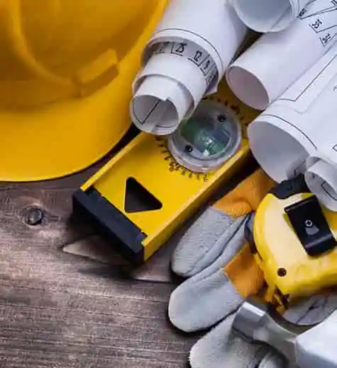 Construction tools including gloves, alignment tool, and building blueprints on a work table